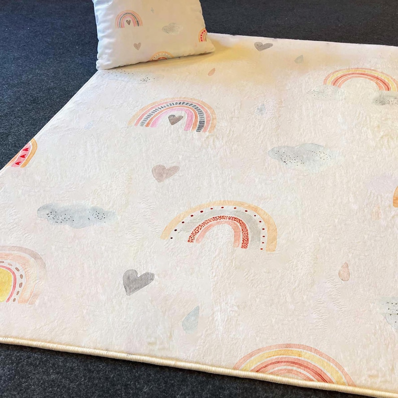 May include: A white plush rug with a repeating pattern of colorful rainbows, clouds, and hearts. The rug has a cream-colored border.