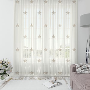 May include: White sheer curtains with embroidered beige stars. The curtains are hanging in a living room with a couch and a floor lamp.
