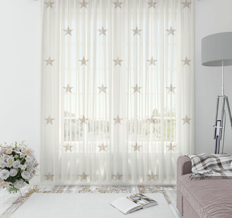 May include: White sheer curtains with embroidered beige stars. The curtains are hanging in a living room with a couch and a floor lamp.