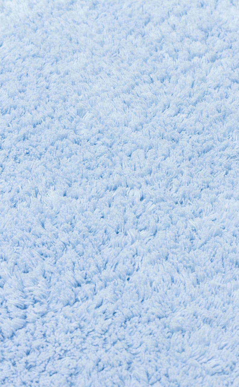 May include: Close-up of a light blue fluffy bath mat. The texture is soft and plush.