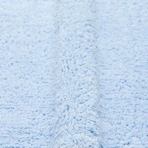 May include: A light blue bath mat made of soft, fluffy material. The mat is folded in half, showing the texture of the fabric.