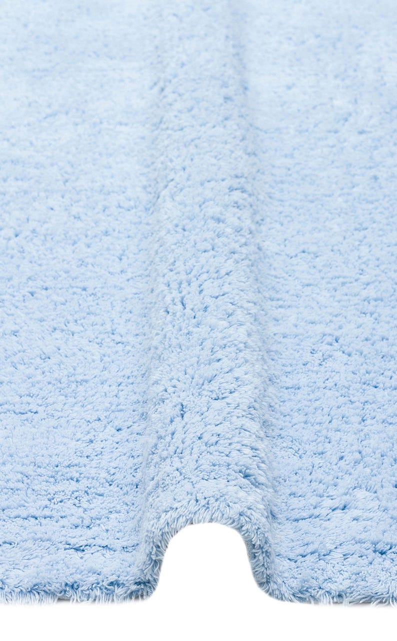 May include: A light blue bath mat made of soft, fluffy material. The mat is folded in half, showing the texture of the fabric.