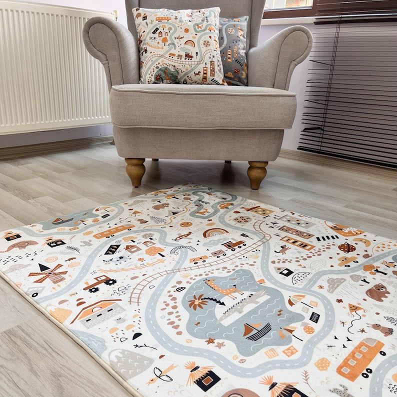 Puede incluir: Una alfombra de juego para ni&ntilde;os con un dise&ntilde;o de mapa de carreteras que presenta coches, trenes y barcos en tonos azules, naranjas y marrones. Dos cojines a juego descansan sobre un sill&oacute;n beige. La alfombra es rectangular.