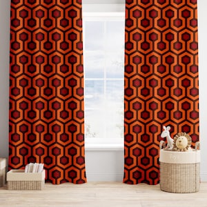 May include: A pair of orange and red curtains with a geometric pattern. The curtains are hung in a window with a white frame. A wicker basket with the word "Toys" on it is in the foreground.