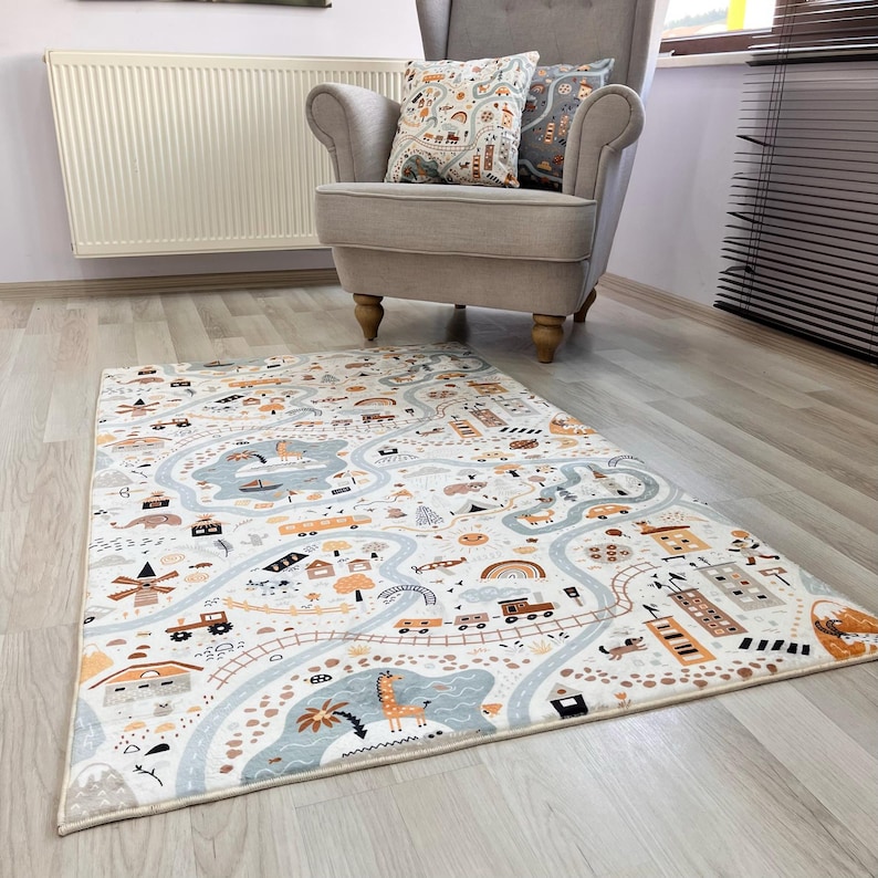 Puede incluir: Una alfombra de juego rectangular con un dise&ntilde;o de mapa de carreteras. La alfombra presenta carreteras, edificios, veh&iacute;culos y animales en tonos de azul, naranja y marr&oacute;n sobre un fondo blanco. Un sill&oacute;n gris y cojines decorativos est&aacute;n en el fondo.