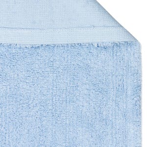 May include: A light blue bath mat with a soft, fluffy texture. The mat has a woven edge.