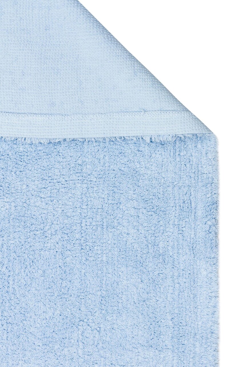 May include: A light blue bath mat with a soft, fluffy texture. The mat has a woven edge.
