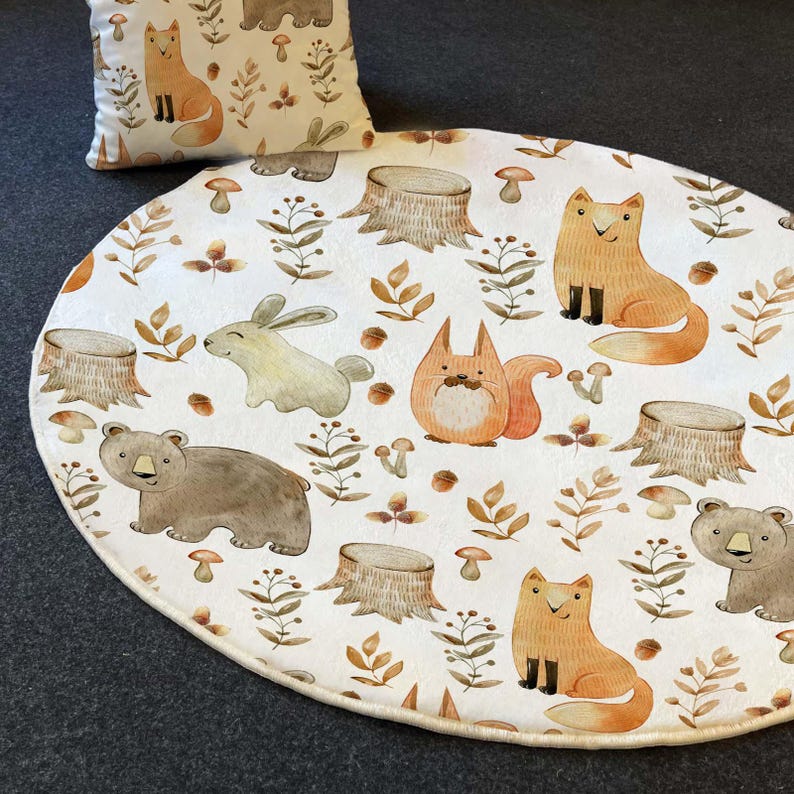 May include: A white round play mat with a woodland theme. The mat features a variety of animals including foxes, bears, squirrels, and rabbits. The animals are surrounded by trees, leaves, and mushrooms.