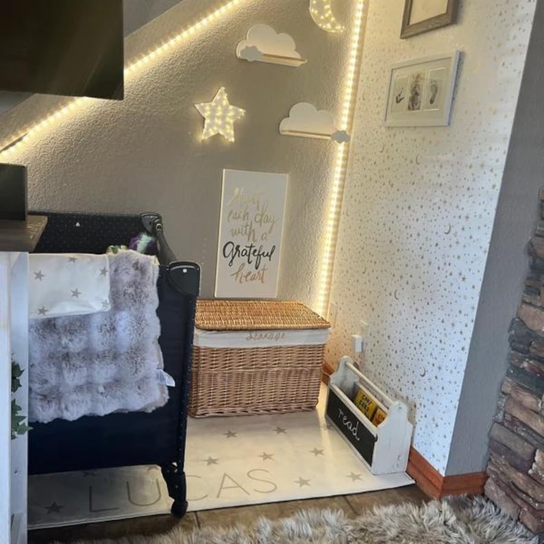 May include: A nursery room with a crib, a wicker storage basket, a wooden sign with the text "Live each day with a grateful heart", and a white rug with gold stars and the name "Lucas" printed on it.