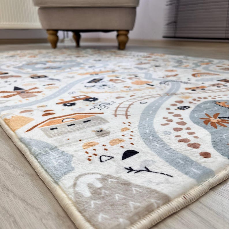 Puede incluir: Alfombra de juego para ni&ntilde;os con dise&ntilde;o de carretera y ciudad. La alfombra presenta un fondo crema con carreteras, edificios y otros elementos en tonos azules, marrones y naranjas. La alfombra es rectangular y tiene un borde crema.