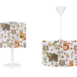May include: Two white lampshades with a woodland animal print. The lampshades feature a brown bear, a fox, a squirrel, and a rabbit. The print is in watercolor style and has a light brown background.