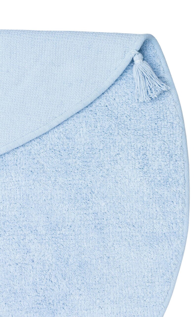 May include: A light blue round bath mat with a tassel on the edge.