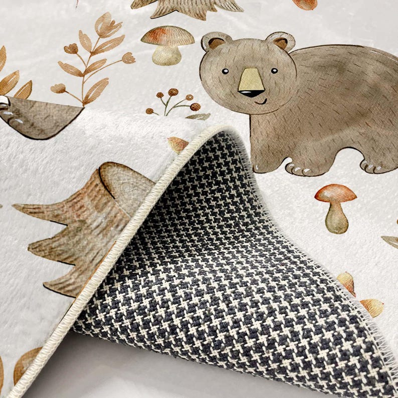 May include: A white rug with a brown bear, mushrooms, and leaves printed on it. The rug has a gray non-slip backing.
