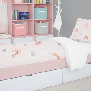 May include: A pink twin-sized bed with a white and pink rainbow patterned duvet cover and a matching pillow. The bed has a white headboard and footboard with storage drawers. The bed is in a room with a pink bookshelf and a white unicorn stuffed animal.