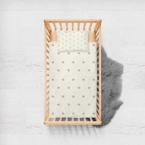 May include: A wooden crib with a white and brown star patterned bedding set. The bedding includes a fitted sheet and a pillowcase.