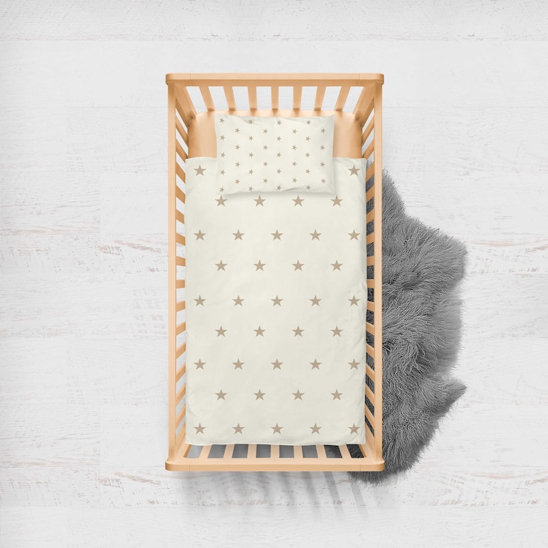May include: A wooden crib with a white and brown star patterned bedding set. The bedding includes a fitted sheet and a pillowcase.