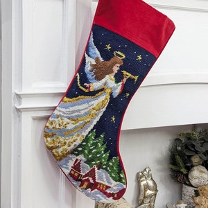 May include: Two Christmas stockings hanging on a white fireplace mantel. The stocking on the left features an embroidered angel with a trumpet, while the stocking on the right features an embroidered Santa Claus with a reindeer.