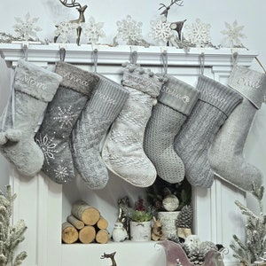 May include: A set of eight grey and white Christmas stockings with personalised names, including "Mom", "Anna", "Papa", "Mike", "Stella", "Nana", and "Dad". The stockings are hanging on a white fireplace mantel with decorative reindeer and snowflakes.