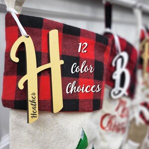 May include: Red and black buffalo plaid Christmas stocking with a wooden personalized name tag that says "Heather". The stocking has a white tag that says "12 color choices".