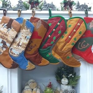 Puede incluir: Seis calcetines de Navidad con forma de bota vaquera de colores con varios diseños bordados, incluyendo caballos, acebo y herraduras. Los calcetines están colgados en una repisa blanca.