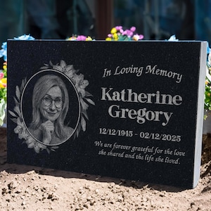 May include: A black granite memorial plaque with the inscription "In Loving Memory Katherine Gregory 12/12/1945 - 02/12/2025". It features a portrait within a floral wreath and a heartfelt message.