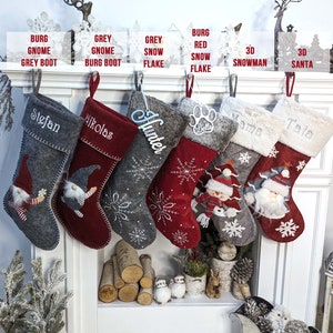 Puede incluir: Una colecci&oacute;n de calcetines navide&ntilde;os en varios colores y dise&ntilde;os, colgados sobre una chimenea. Los calcetines son grises y rojos, con nombres personalizados y adornos festivos como copos de nieve, gnomos y mu&ntilde;ecos de nieve. El texto sobre los calcetines dice "BURG GNOME GREY BOOT", "GREY GNOME BURG BOOT", "GREY SNOW FLAKE", "BURG RED SNOW FLAKE", "3D SNOWMAN" y "3D SANTA".