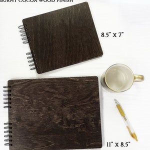 Puede incluir: Dos cuadernos con espiral con acabado de madera de cacao quemado. Uno mide 28 x 22 cm, el otro 22 x 18 cm. Tambi&eacute;n hay una taza blanca con asa dorada y un bol&iacute;grafo dorado y transparente.