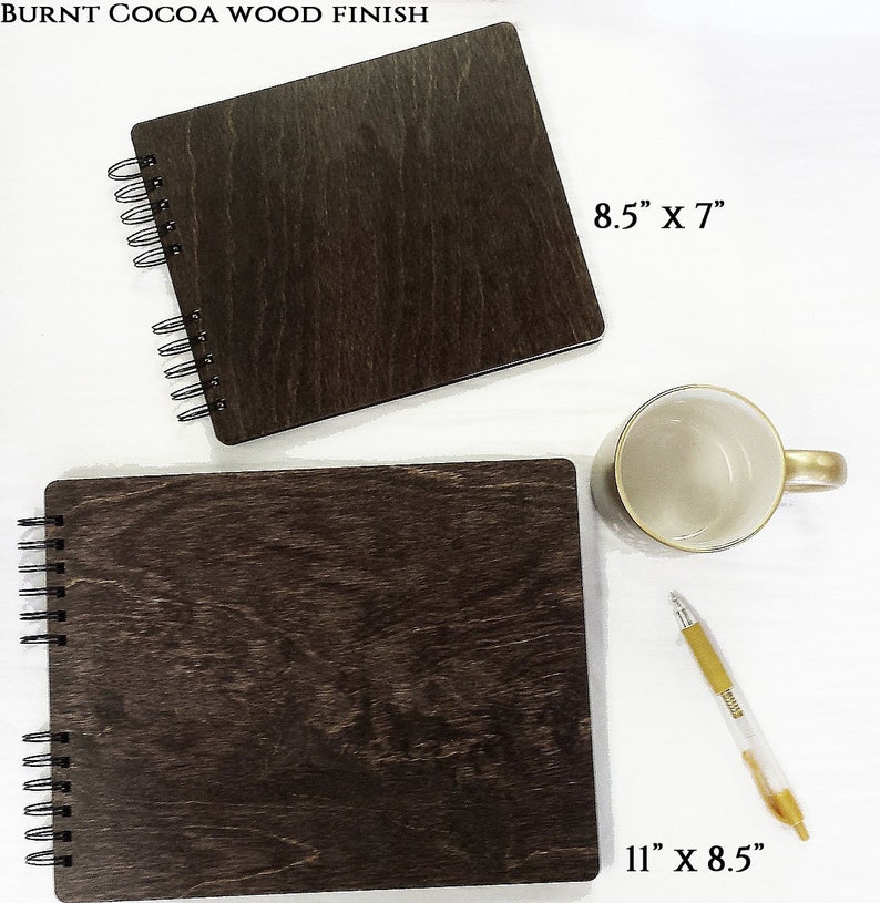 Puede incluir: Dos cuadernos con espiral con acabado de madera de cacao quemado. Uno mide 28 x 22 cm, el otro 22 x 18 cm. Tambi&eacute;n hay una taza blanca con asa dorada y un bol&iacute;grafo dorado y transparente.