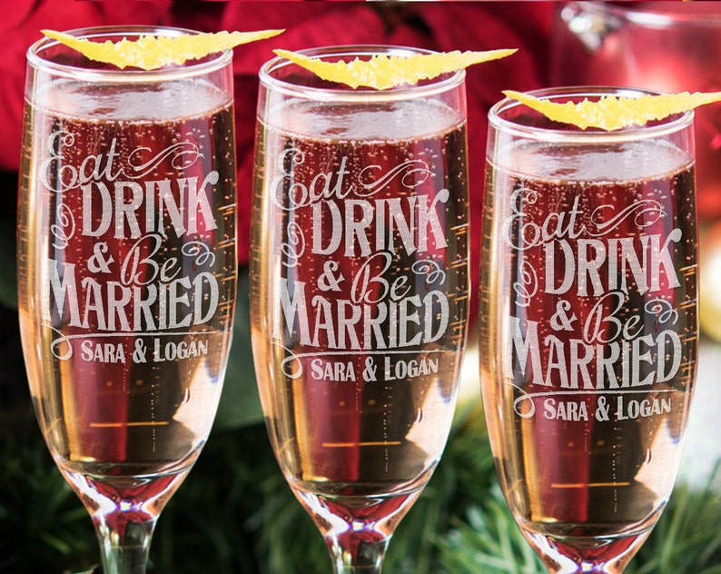 Puede incluir: Tres copas de champ&aacute;n con el texto "Eat Drink & Be Married" y los nombres "Sara & Logan" grabados en la parte delantera.