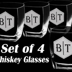 Puede incluir: Juego de cuatro vasos de whisky con base cuadrada y forma &uacute;nica. Cada vaso presenta un hex&aacute;gono blanco con las iniciales "BT" en una fuente serif. El texto "Set of 4 Whiskey Glasses" se muestra debajo.
