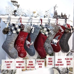 Puede incluir: Una colecci&oacute;n de calcetines navide&ntilde;os en varios colores y dise&ntilde;os, colgados de una repisa blanca. Los calcetines incluyen patrones de cuadros, copos de nieve y gnomos, con etiquetas de nombre personalizadas. Los colores incluyen gris, burdeos y rojo.