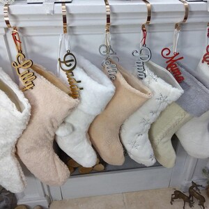May include: Seven white and cream-colored stockings with gold and red personalized name tags. The names on the tags are "Wyatt", "Lilly", "Daddy", "Kellie", "Pizza", "Mama", and "Charles".