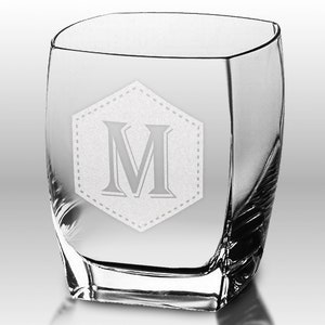 Puede incluir: Un vaso transparente de forma cuadrada con un dise&ntilde;o curvo. El vaso presenta un dise&ntilde;o grabado de la letra "M" dentro de un hex&aacute;gono punteado. El vaso es adecuado para bebidas.