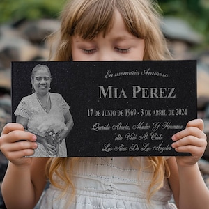May include: A black granite memorial plaque with a silver inscription. The inscription reads "En memoria Amorosa MIA PEREZ 17 DE JUNIO DE 1969-3 DE ABRIL DE 2024 Querida Abuela, Madre Y Hermana ella Voló Al Cielo Las Alas De Los Angeles". A photo of a woman is in the top left corner of the plaque.