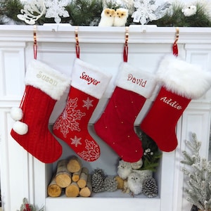 May include: Four red Christmas stockings with white faux fur cuffs hang from a mantel. Each stocking is personalized with a name embroidered in a contrasting color: Susan, Sawyer, David, and Addie. The stockings are decorated with snowflakes and pom-poms.