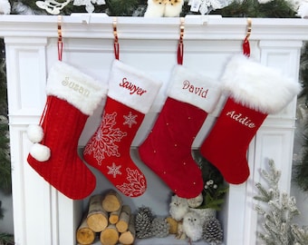 May include: Four red Christmas stockings with white faux fur cuffs hang from a mantel. Each stocking is personalized with a name embroidered in a contrasting color: Susan, Sawyer, David, and Addie. The stockings are decorated with snowflakes and pom-poms.