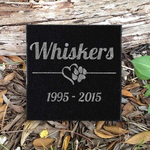 May include: Black granite pet memorial with the name "Whiskers" engraved, a heart with a paw print, and the dates "1995 - 2015".