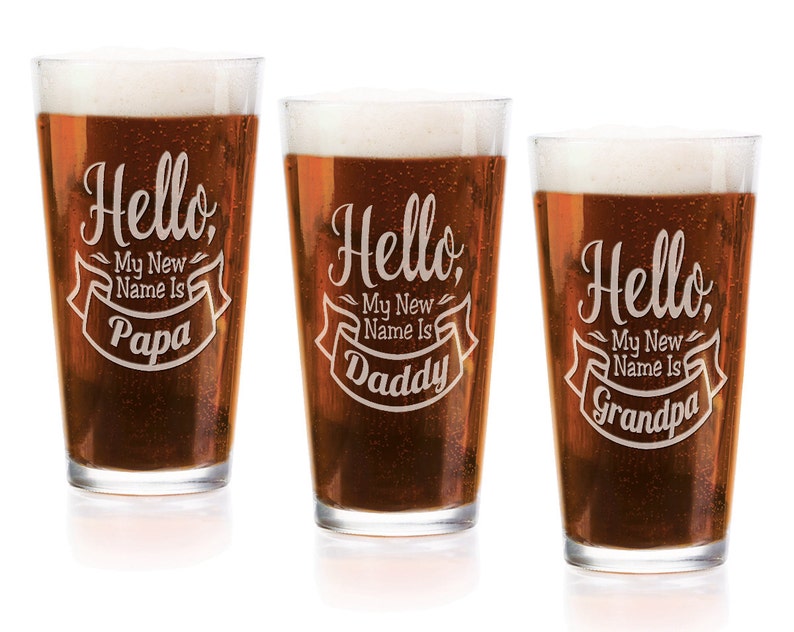 May include: Three clear glass pint glasses filled with amber beer and white foam. Each glass features white etched text that reads Hello, My New Name Is followed by the words Papa, Daddy, or Grandpa inside a decorative banner graphic.