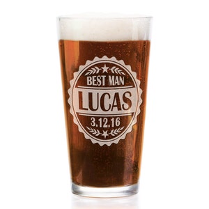 May include: A clear glass beer mug with a brown liquid inside. The mug has a white design with the text "Best Man Lucas 3.12.16" in a circle.