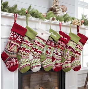 Könnte beinhalten: Sieben gestrickte Weihnachtsstrümpfe in Rot, Grün und Weiß mit verschiedenen Mustern, darunter Schneeflocken und der Weihnachtsmann. Einige sind mit den Wörtern "Dad" und "Mom" personalisiert. Sie hängen an einem Kaminsims.