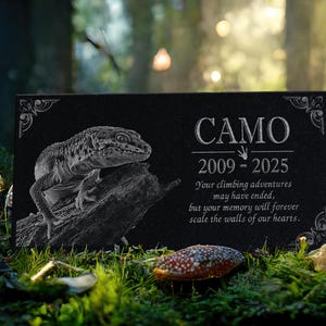 May include: Black granite pet memorial with a white engraved gecko lizard and the text "CAMO 2009-2025 Your climbing adventures may have ended, but your memory will forever scale the walls of our hearts."