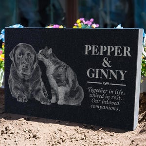 May include: Black granite pet memorial with a photo of a black dog and a cat. The inscription reads "Pepper & Ginny Together in life, united in rest. Our beloved companions."
