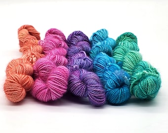 Könnte beinhalten: Eine Sammlung farbenfroher Garnknäuel in einem Farbverlauf von Orange über Pink und Lila bis hin zu Blau und Grün. Das Garn ist fest gewickelt und wirkt weich, ideal für Strick- oder Häkelprojekte. Die Knäuel liegen auf weißem Grund.