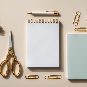 May include: A flat lay of office supplies on a beige background. The items include a spiral bound notebook, a gold pen, a pair of gold scissors, gold paper clips, and a dried flower.