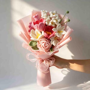 May include: A handcrafted bouquet of crochet flowers in shades of pink, red, white, and yellow. The bouquet is wrapped in pink paper and tied with a sheer ribbon. The flowers include roses, tulips, and other floral designs.