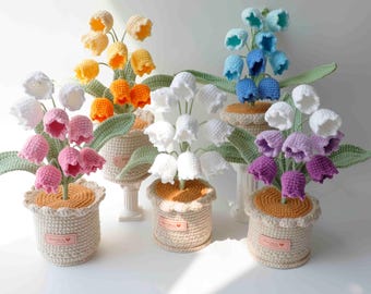 May include: A collection of handmade crochet lily of the valley flowers in various colors, including white, pink, yellow, orange, blue, and purple. Each flower is potted in a beige crochet pot with green leaves, creating a charming display.