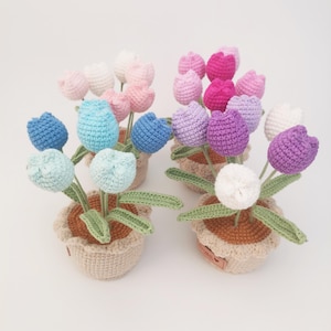 May include: Five crocheted flower pots with different coloured flowers. The flowers are all in the shape of tulips and are in shades of pink, purple, blue, and white. The pots are all brown and have a crocheted design.