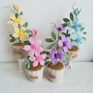 May include: Three crocheted flower arrangements in pots. The flowers are yellow, pink, and light blue. The pots are beige with brown trim and a label that says "Hand Made".