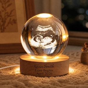 May include: A glass sphere displaying an ultrasound image, illuminated from within and set on a wooden base. The base is engraved with the text "Kevin Smith, Love Begins, April 2026". The warm light creates a comforting glow, a sentimental keepsake.