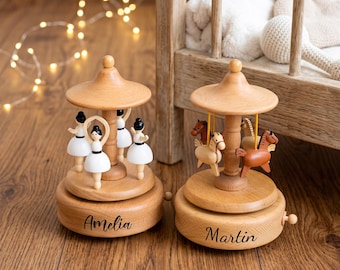 May include: Two wooden carousel music boxes with natural light wood finishes. One features four white-clad ballerinas and the name Amelia, while the other features four small brown and tan horses and the name Martin, both with circular bases.